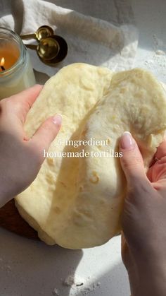 two hands are holding a piece of bread in front of a candle and some napkins