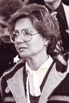 an old black and white photo of a woman with glasses sitting in front of other people