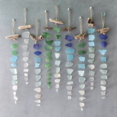 several pieces of sea glass hanging from hooks on a gray wall with birds and seashells attached to them