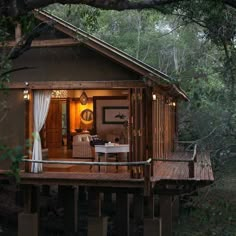 a small cabin in the middle of some trees with curtains on it's windows