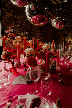 the table is set with pink and red flowers, silverware, candles, and wine glasses