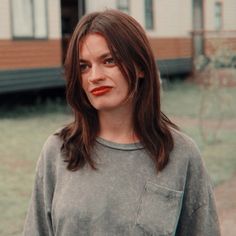 a woman standing in front of a house with red lipstick on her face and long hair