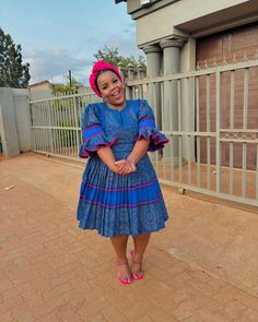 a woman standing in front of a gate wearing a blue dress and pink head scarf