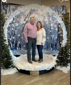 a man and woman standing in front of a backdrop for a christmas photo shoot with snow on the ground