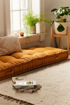 an orange futon sofa in front of a window with potted plants on it