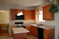 an empty kitchen with wooden cabinets and black appliances in the center, along with white counter tops