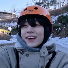 a young man wearing a helmet while standing in front of snow covered hills and trees