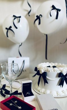 a white cake sitting on top of a table next to some wine glasses and balloons