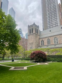 a large building sitting in the middle of a lush green park next to tall buildings