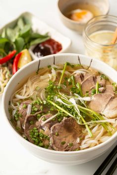 a white bowl filled with meat and veggies next to chopsticks on a table