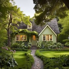 a green house surrounded by lush green trees and bushes with white flowers on the front