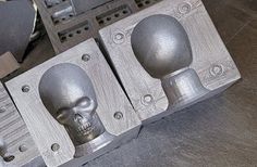 two metal skull heads are attached to the side of a machined tool box with holes in it