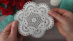 a person holding up a piece of white crocheted doily next to red roses