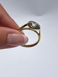 a woman's hand holding a gold ring with an oval shaped diamond on it