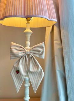 a white lamp with a bow on it next to a blue curtain and a light shade