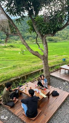 four people sitting at a picnic table in the middle of an open area with green fields behind them