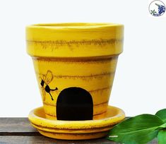 a yellow flower pot with a black hole in the middle and green leaves around it