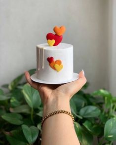 a hand holding a white cake with hearts on it