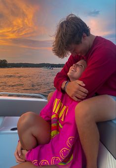 a man and woman sitting on the back of a boat in front of a sunset