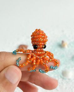 an orange beaded octopus is held in someone's hand