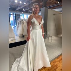 a woman in a white dress standing on a wooden floor next to a rack of wedding dresses