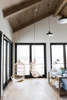 two hanging chairs in the middle of a room with large windows and wooden ceiling beams