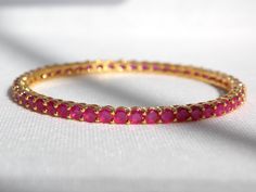 Designed in the USA, handcrafted with love by our female artisans in India this beautiful Bangle Set comes in a gold plated finish with stunning Red Ruby lab grown stones to make this exquisite Bangle Set really special - light in weight & can be paired with almost any outfit. Perfect accessory for every jewelry box!  - Handcrafted  - Metal: Metal Alloy, Gold Plated  - Stone: American Diamond (Lab Grown), Ruby CZ Stones (Lab Grown)  - Size: Size 2.8 (2.5" interior width), Fits Most Wrist Sizes  - Set of 4 Bangles Please care for your product by refraining from exposing items to harsh chemicals and abrasives, water, alcohol or constant direct sunlight.  Please store items in provided padded box.  A soft cloth and gentle swipe will bring your items back to luster once removed for next time u Wedding Bangle With Gemstone, Gold Plated Round Bangle For Wedding, Adjustable Gemstone Bangle For Wedding, Gold Ruby Stackable Jewelry, Gemstone Round Bangle For Wedding, Gold Gemstone Bangle For Anniversary, Ruby Gold Bangle For Celebration, Gold Ruby Bangle For Celebration, Ruby Gemstone Bangle For Wedding