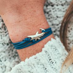 a woman wearing a blue bracelet with a shark charm on it's wrist,