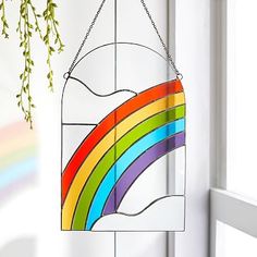 a rainbow stained glass hanging on the side of a white door with a green plant in front of it