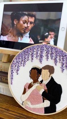 an embroidered picture of a man and woman in love on a tabletop next to some books