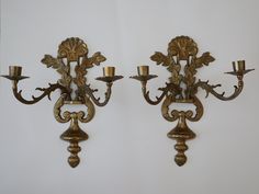 two golden wall sconces with candles on them against a white wall in a room