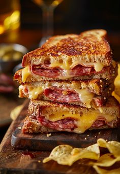 a grilled cheese and ham sandwich on a cutting board with potato chips next to it