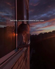 a woman is looking out the window at sunset