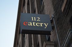 a sign that reads 12 eatery hanging from the side of a tall brick building