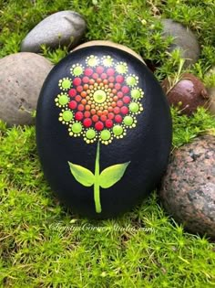 a painted rock with a flower on it sitting in the grass next to some rocks