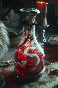 a red and white vase sitting on top of a wooden table next to a candle