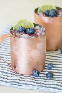 two copper mugs filled with blueberries and lime on top of a striped napkin