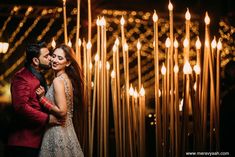 a man and woman standing next to each other in front of some lights with candles behind them