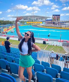 a woman standing on top of a blue chair in front of a stadium filled with people