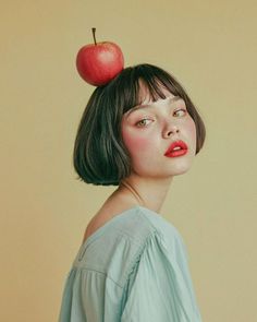 a woman with an apple on top of her head, in front of a beige background