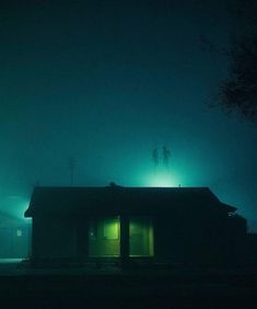 two people standing on the roof of a house in the dark with green light coming from their windows