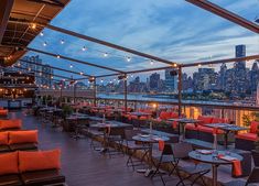 an outdoor dining area with tables and chairs overlooking the city skyline at night, lit by string lights