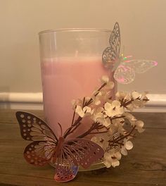 a glass filled with pink liquid sitting on top of a wooden table next to a butterfly decoration