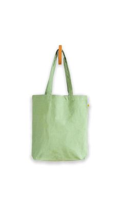 a green tote bag hanging from a hook on a white wall with an orange handle