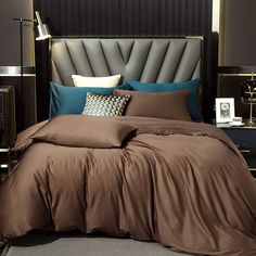 a bed with brown sheets and blue pillows in a dark colored room, next to a night stand