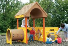 two adults and three children playing in a play area with a yellow structure, brown roof and orange walls