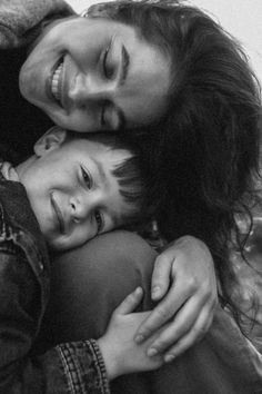 a woman and child hugging each other while they are smiling at the camera, black and white photograph