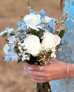 a woman in a blue dress holding a bouquet of white roses and blue hydrangeas