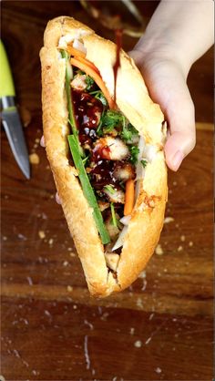 a person holding a sandwich with meat and veggies in it on a wooden table