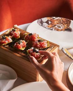 a person reaching for food in a wooden box on a table with plates and utensils